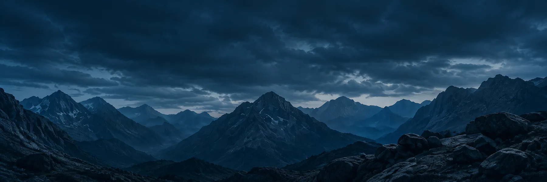 Layered mountain ridges beneath a dark blue clouded sky.